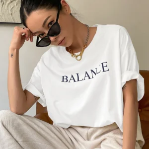 Woman wearing white oversized 'Balance' graphic print cotton t-shirt with loose fit and short sleeves.