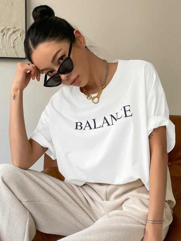 Woman wearing white oversized 'Balance' graphic print cotton t-shirt with loose fit and short sleeves.