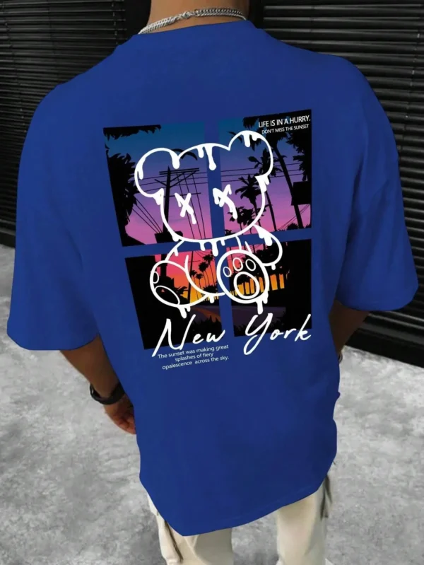 Men's loose fit cotton t-shirt displaying a colorful graphic print of a cartoon bear in front of a New York sunset scene.