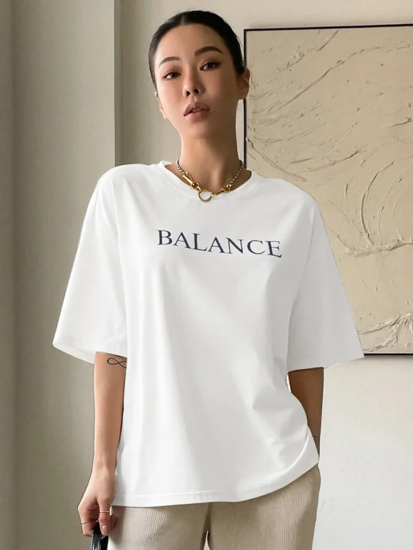 Woman wearing white oversized 'Balance' graphic print cotton t-shirt with loose fit and short sleeves.