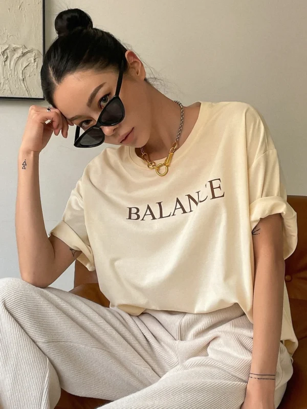 Woman wearing white oversized 'Balance' graphic print cotton t-shirt with loose fit and short sleeves.