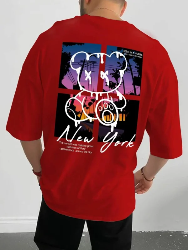 Men's loose fit cotton t-shirt displaying a colorful graphic print of a cartoon bear in front of a New York sunset scene.