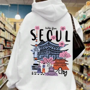 Woman wearing a comfortable warm fleece hoodie with a scenic Seoul print design and artificial fur lining visible inside the hood.
