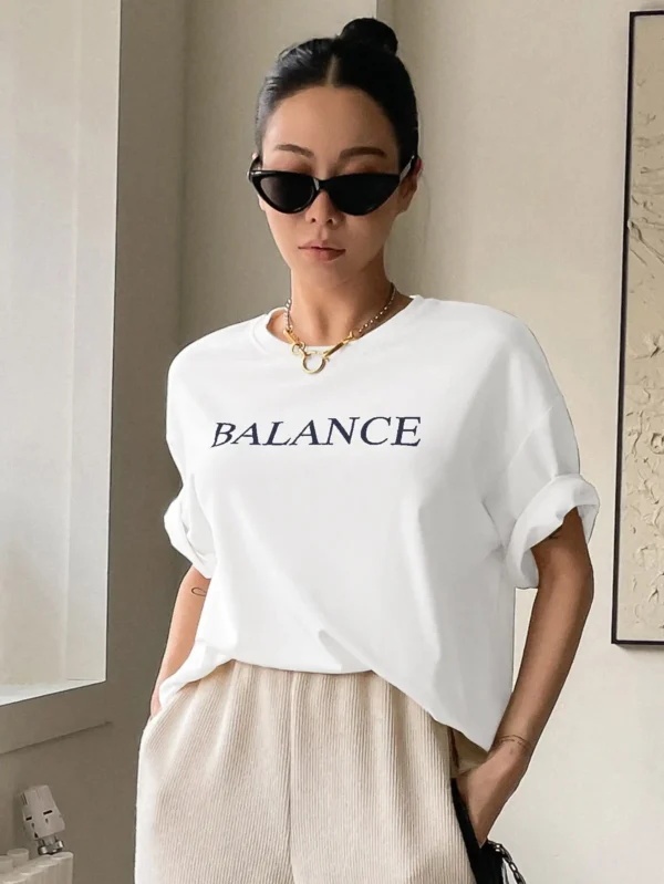Woman wearing white oversized 'Balance' graphic print cotton t-shirt with loose fit and short sleeves.